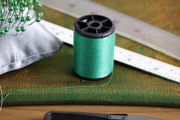 Place a small spool of green thread between the pincushion and the ruler on a large piece of fabric of the same color.
