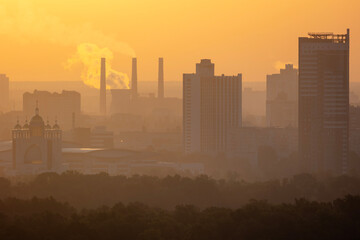 Greek Catholic Cathedral and industrial skyline with smoke at sunrise. Hazy morning cityscape under golden sky over Dnipro river districts in Kyiv city with copy space and urban atmosphere.