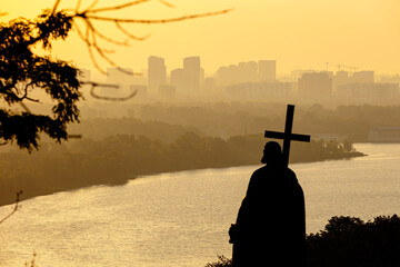 Saint Volodymyr Monument silhouette with cross overlooking Dnipro river at sunrise. Hazy city...