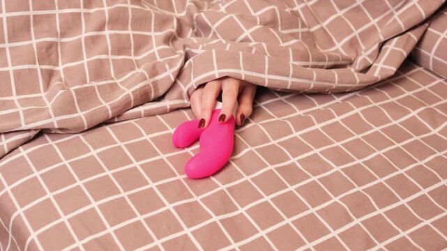 A womans hand reaches out from under the blanket for a vibrator. A woman takes an adult toy to satisfy herself.