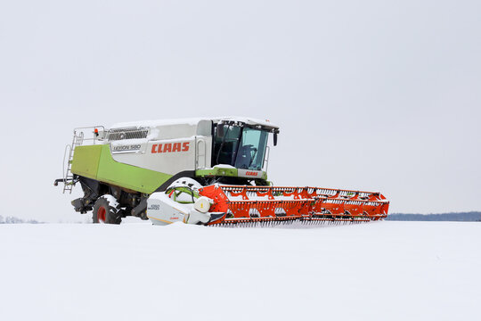 Lviv, Ukraine - January 07, 2026: ​A Claas Lexion 580 combine harvester with a massive orange header stands still in the middle of a vast field covered in a thick layer of fresh snow.