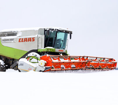 Lviv, Ukraine - January 07, 2026: The powerful cab and bright orange header of a Claas Lexion 580 combine are captured in a close-up amidst deep white snow.