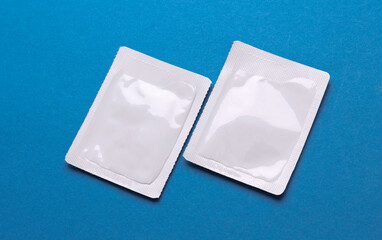 Blank white sachet packets mockup on blue background. Empty disposable shampoo or conditioner pack mock up