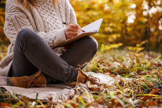 Woman sitting on blanket in autumn forest writing diary. Journaling for good mental wellbeing and mindfulness intentions