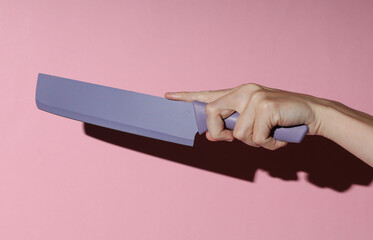 Ceramic kitchen knife in a female hand on a pink backgroun