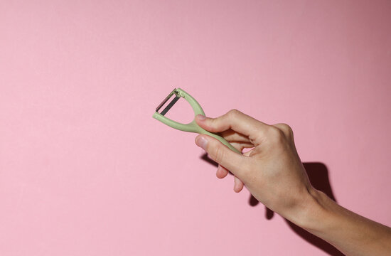 Hand holding Kitchen peeler knife for peeling vegetable skins on pink background