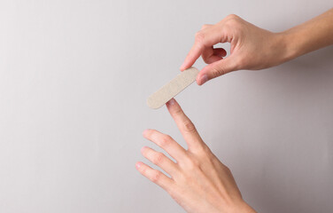 Woman files her fingernails with a nail file in hand on gray background