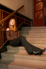A young beautiful woman sits on the stairs in the entrance of an old house