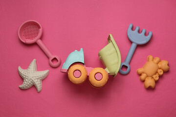 Children's dump truck with sandbox toys on pink background. Flat lay