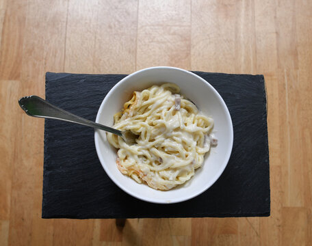Schlichte Sch&uuml;ssel mit Nudeln und heller Sauce auf dunkler Unterlage vor neutralem Hintergrund. Das Motiv steht f&uuml;r einfache K&uuml;che, Minimalismus, Alltag und puren Genuss. Mikrowelle aufw&auml;rmen fastfood