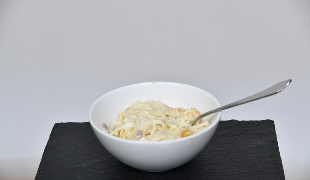 Schlichte Sch&uuml;ssel mit Nudeln und heller Sauce auf dunkler Unterlage vor neutralem Hintergrund. Das Motiv steht f&uuml;r einfache K&uuml;che, Minimalismus, Alltag und puren Genuss. Mikrowelle aufw&auml;rmen fastfood