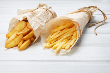 Potato wedges and french fries wrapped in brown wrapping paper. Fast food take away at white shabby...