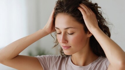 Fototapeta premium Young woman with her eyes closed, holding her head with both hands. she appears to be in pain or discomfort, with her hair pulled back in a messy bun.