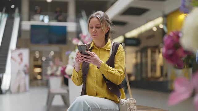 Woman using smartphone in modern shopping mall.