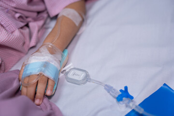 Close up of a patient hand with an intravenous IV drip needle and fluid infusion on a hospital bed. Concept of healthcare, medical treatment, emergency room, and hospital admission
