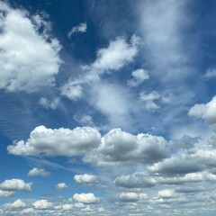 Fototapeta premium Daytime sky with soft white clouds drifting across a blue background. Natural cloudscape illuminated by daylight, creating a calm and peaceful atmosphere.