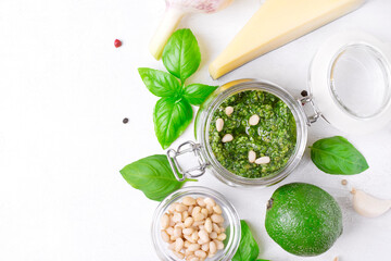 Pesto sauce in glass jar and ingredients for cooking it on white. Copy space