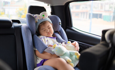 Little Asian girl sleeping peacefully in a car seat during a road trip,A cute young Asian girl wearing a headband is fast asleep in her safety car seat while traveling in a vehicle,