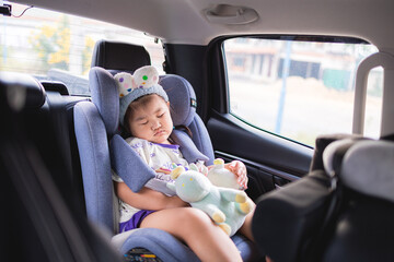 Little Asian girl sleeping peacefully in a car seat during a road trip,A cute young Asian girl wearing a headband is fast asleep in her safety car seat while traveling in a vehicle,