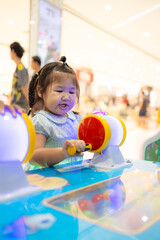 Little Asian girl playing interactive arcade game at indoor playground,A cute little Asian girl with braided hair concentrates on playing a colorful interactive arcade game at a children's amusement 