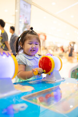 Little Asian girl playing interactive arcade game at indoor playground,A cute little Asian girl with braided hair concentrates on playing a colorful interactive arcade game at a children's amusement 
