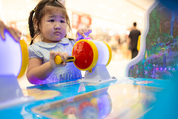 Little Asian girl playing interactive arcade game at indoor playground,A cute little Asian girl with braided hair concentrates on playing a colorful interactive arcade game at a children's amusement 