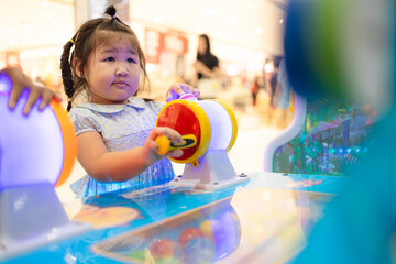 Little Asian girl playing interactive arcade game at indoor playground,A cute little Asian girl with braided hair concentrates on playing a colorful interactive arcade game at a children's amusement 