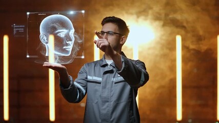 A man in a gray jumpsuit interacts with a translucent holographic human head projection in a futuristic setting with glowing lights