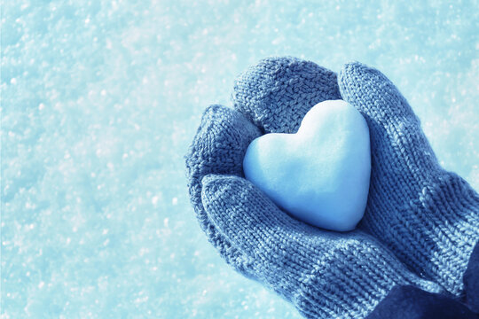 Hands in knitted mittens hold heart of snow in winter day. Love concept. Valentine day concept.	