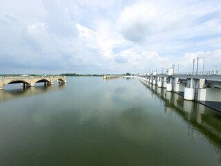Wide view of old broken and new structure in Mukkombu Dam (Upper Anaicut) arches stretching across the Kaveri river waters under cloudy skies in Tiruchirappalli district, Tamil Nadu.