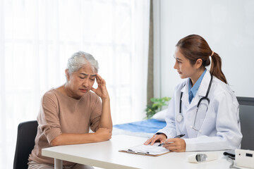 Doctor consulting with an elderly woman experiencing headache and stress symptoms, discussing...