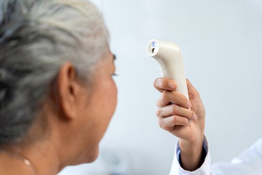 Healthcare worker checking senior woman's temperature using a non contact infrared thermometer for fever screening and health monitoring