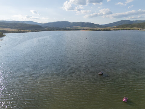 Aerial view of the serene Ruzina water dam reflecting the sky, framed by verdant hills under a sky dotted with fluffy clouds, Ruzina, Banska Bystrica Region, Slovakia.
