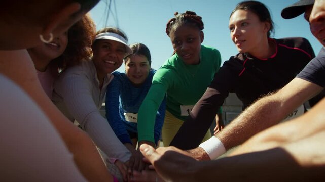 A group of happy runners huddle together, placing their hands in the center before raising them in a gesture of unity and motivation. They are ready for a race.