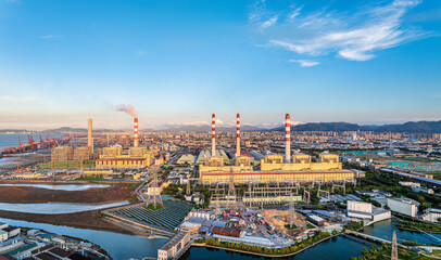 Large thermal power plant and industrial zone with city skyline in the background under a clear blue sky.