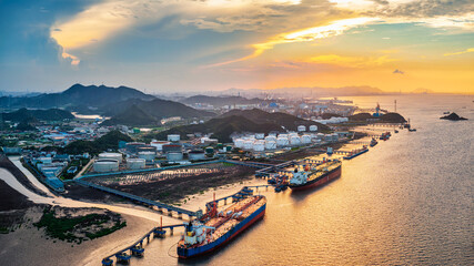 Large oil tankers docked at a coastal refinery and storage terminal during sunset. © zhao dongfang