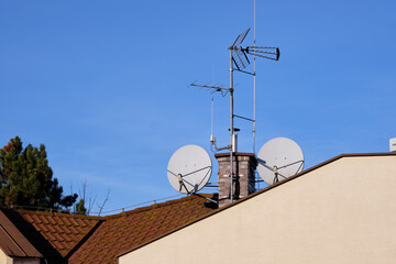 Against a vibrant blue sky, antennas and satellite dishes stand atop a brick chimney on a rooftop. The scene unfolds on a sun-drenched day, casting an aura of clear reception