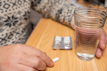 Tablet on a wooden table next to a glass of water and blister pack. Represents daily medication routine and home healthcare concept.