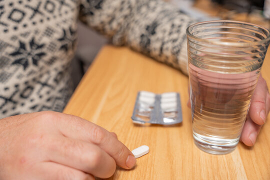 Tablet on a wooden table next to a glass of water and blister pack. Represents daily medication routine and home healthcare concept.