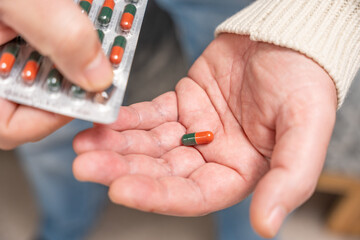 Close-up of hands pushing a capsule from a blister pack into the palm. Symbolizes correct medication use and pharmaceutical treatment.
