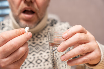 Man opening mouth while holding a tablet and water glass. Concept of swallowing medication and following medical treatment instructions.