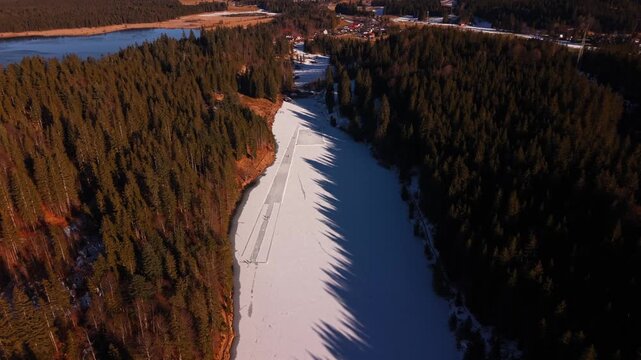 Vogelperspektive auf den Grubsee im Landkreis Garmisch-Partenkirchen. Menschen geniessen Wintersport auf dem Natureis. Cineastischer Blick auf verschneite Waelder und das Wettersteingebirge