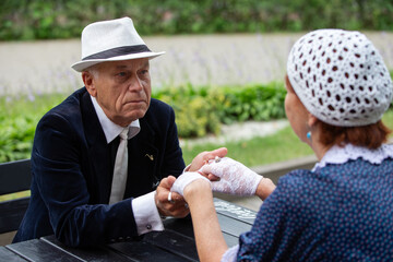 Elderly man and woman engage in a friendly arm wrestling match in a sunny garden setting