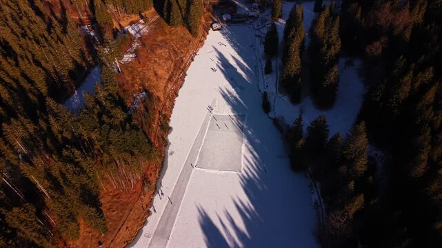 High-altitude drone shot of the snow-covered Grubsee area. People glide across the frozen lake surface. A scenic landscape featuring the Karwendel mountains and a dense winter forest.