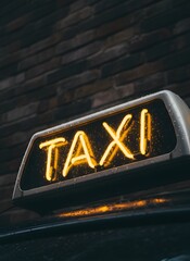 Illuminated neon TAXI sign with raindrops on a car roof against a blurred dark brick wall background.