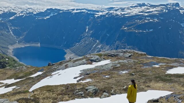 Hiker walking across snowy plateau near Trolltunga, Norway. Beautiful woman exploring high mountain terrain above the fjord during a summer hiking trip.
