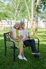 Happy senior Asian couple laughing and relaxing together on a park bench in a sunny outdoor garden