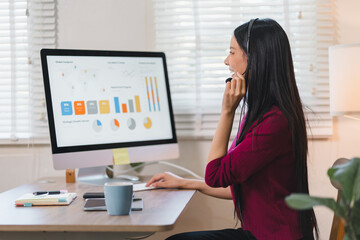 Asian business woman wearing a customer service headset while working on data analysis for remote work in her home office