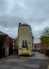 A narrow street with buildings on either side, including a tall, yellow building with a balcony.