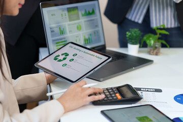 Professional business woman analyzes ESG data for a sustainable future using a digital tablet and calculator in an office.